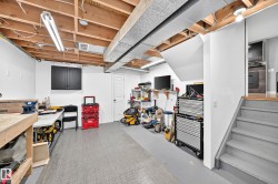 Finished basement space featuring exposed ceiling joists, overhead fluorescent lighting, and a neutral-toned floor - 