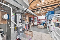 Utility area featuring exposed ceiling joists and ductwork, a water heater, a furnace, and white wall cabinetry - 