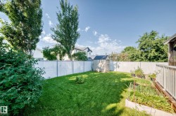 Spacious backyard featuring a manicured lawn, a white chain-link fence, a storage shed, and raised garden beds - 