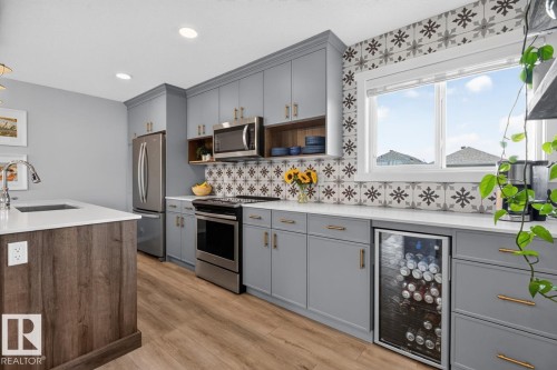 Open Concept Kitchen featuring Stainless Steel Appliances, Stylish Lighting and Accent Tiles, Bar Fridge, and Bar/Counter Seating. - 1051 Cy Becker Road Nw, Edmonton, AB - Indoor Photo Showing Kitchen With Upgraded Kitchen