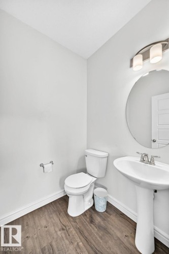 Powder room featuring a pedestal sink with a chrome faucet, a circular mirror, and a three-light vanity fixture - 1261 Rosenthal Boulevard Nw, Edmonton, AB - Indoor Photo Showing Bathroom