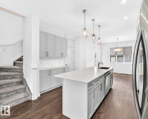 Modern kitchen featuring an island with a built-in sink, stainless steel appliances, light gray cabinetry, and a white herringbone tile backsplash - 1261 Rosenthal Boulevard Nw, Edmonton, AB - Indoor Photo Showing Kitchen With Upgraded Kitchen