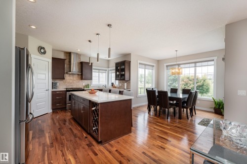 Spacious kitchen and dining area featuring wood-finish flooring, a kitchen island with a light-toned countertop, dark wood cabinetry, stainless steel appliances, and multiple windows - 2338 Frezenberg Avenue Nw, Edmonton, AB - Indoor