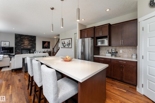 Kitchen island featuring a light-toned countertop, stainless steel pendant lighting, wood-finish flooring, and dark wood cabinetry with stainless steel appliances - 2338 Frezenberg Avenue Nw, Edmonton, AB - Indoor
