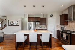Kitchen featuring a central island with white countertop, rich wood-finish cabinetry, stainless steel appliances, and a tiled backsplash - 