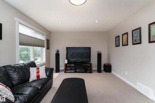 Carpeted entertainment space featuring a large window with privacy blinds, recessed lighting, and crown molding - 2338 Frezenberg Avenue Nw, Edmonton, AB - Indoor