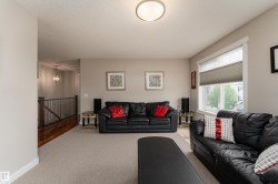 Spacious carpeted living area featuring neutral wall paint, a large window with privacy blinds, and a ceiling-mounted light fixture - 