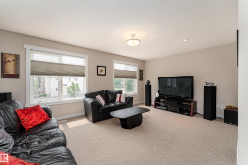Expansive living area featuring neutral carpeting, two large windows with horizontal blinds, and a built-in media console - 2338 Frezenberg Avenue Nw, Edmonton, AB - Indoor Photo Showing Living Room