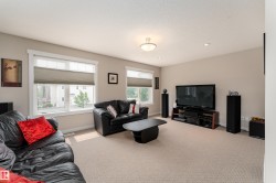 Expansive living area featuring neutral carpeting, two large windows with horizontal blinds, and a built-in media console - 