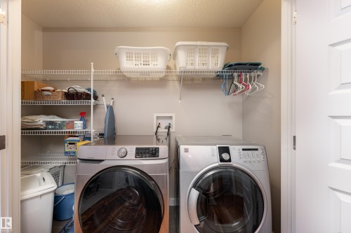 Dedicated laundry area featuring front-loading washer and dryer, integrated wire shelving, and overhead storage - 2338 Frezenberg Avenue Nw, Edmonton, AB - Indoor Photo Showing Laundry Room