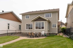 Expansive backyard featuring a manicured lawn, paver patio, stone-clad foundation, bay window, and a shed dormer - 