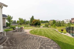 Expansive backyard featuring a circular paver patio, lush green lawn, mature trees, and a decorative black fence - 