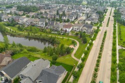 Suburban neighborhood featuring a pond, paved walking paths, residential streets with tree-lined medians, and detached homes with varied architectural styles - 