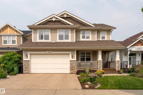 Two-story residence featuring a covered front porch with stone-clad columns, an attached two-car garage, and a textured concrete driveway - 2338 Frezenberg Avenue Nw, Edmonton, AB - Outdoor With Deck Patio Veranda With Facade