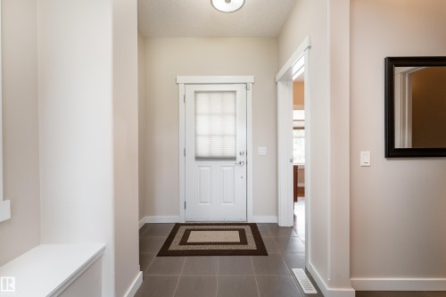 Entryway featuring a white paneled door with integrated blinds, grey square tile flooring, a built-in bench, and a framed wall mirror - 2338 Frezenberg Avenue Nw, Edmonton, AB - Indoor Photo Showing Other Room