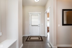 Entryway featuring a white paneled door with integrated blinds, grey square tile flooring, a built-in bench, and a framed wall mirror - 