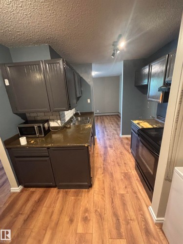 Galley kitchen featuring wood-finish flooring, dark grey cabinetry, and a white subway tile backsplash - #206 2311 119 St Nw, Edmonton, AB - Indoor