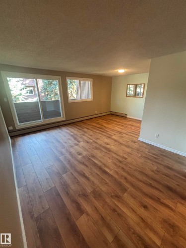 Spacious open-concept room featuring wood-finish flooring, neutral wall tones, and multiple windows - #206 2311 119 St Nw, Edmonton, AB - Indoor Photo Showing Other Room
