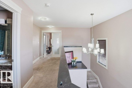 Carpeted hallway with flush-mount ceiling lights, white trim, and a chandelier over the staircase - 258 Albany Drive Nw, Edmonton, AB - Indoor