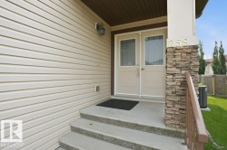 Entryway featuring double doors with decorative glass panels, stone veneer pillar, concrete steps, and a metal handrail - 