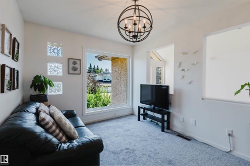 Living area featuring light gray carpeting, an orb-style chandelier with candelabra lights, and a large picture window with white trim - 342 O'Connor Close Nw, Edmonton, AB - Indoor