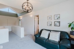 Loft space featuring a vaulted ceiling with triangular window, overhead orb chandelier, and recessed wall sconces - 