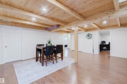 Expansive open-concept room featuring wood-finish flooring, a wood-paneled ceiling with exposed beams, recessed lighting, white paneled doors, and a partial view into an additional room - 