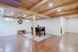 Open-concept room featuring wood-finish flooring, exposed wood beam ceiling, recessed lighting, white walls, and multiple windows - 