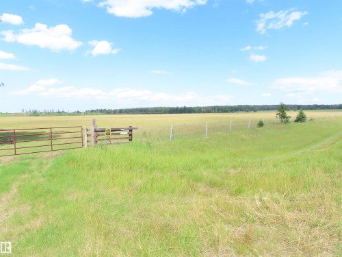 Expansive agricultural land featuring a red metal gate, wire fencing, and mature trees bordering the horizon - 11216 Twp 532, Rural Yellowhead, AB 