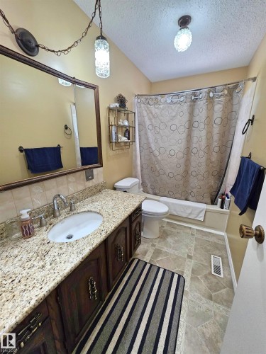 Bathroom featuring a spacious vanity with a granite-look countertop, a built-in sink, and a dark wood-finish cabinet with decorative hardware - 5201 54 Street, Elk Point, AB - Indoor Photo Showing Bathroom