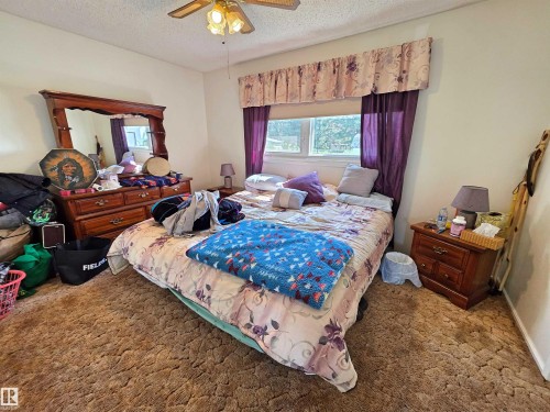 Bedroom featuring textured carpeting, a window with valance and drapes, and a ceiling fan with integrated lighting - 5201 54 Street, Elk Point, AB - Indoor Photo Showing Bedroom