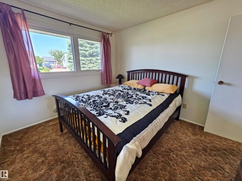 Interior room featuring a large window, neutral wall paint, and a textured carpet - 5201 54 Street, Elk Point, AB - Indoor Photo Showing Bedroom