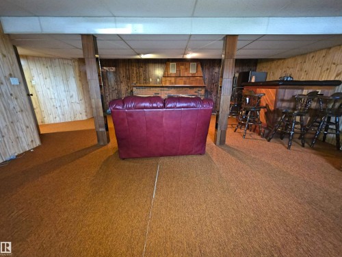 Finished basement featuring a built-in bar with dark wood paneling, wood-finish wall panels, and a drop ceiling - 5201 54 Street, Elk Point, AB - Indoor