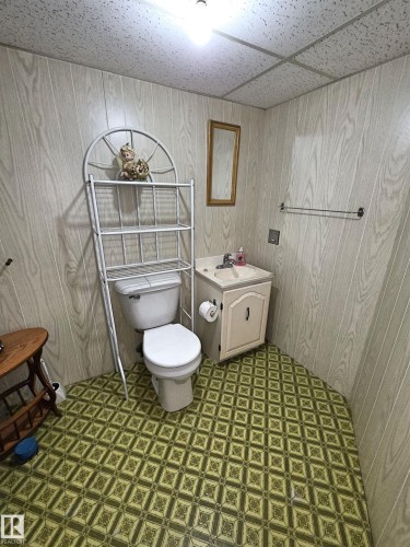 Bathroom featuring wood-finish wall paneling, a white toilet, and a vanity with a surface-mounted sink - 5201 54 Street, Elk Point, AB - Indoor Photo Showing Bathroom