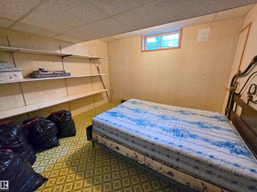 Room featuring textured wall paneling, a drop ceiling, and patterned resilient flooring - 5201 54 Street, Elk Point, AB - Indoor Photo Showing Bedroom