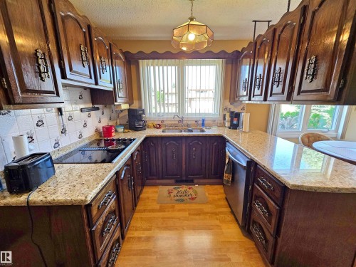 U-shaped kitchen featuring wood cabinetry, light speckled granite countertops, a built-in cooktop, and a double basin sink - 5201 54 Street, Elk Point, AB - Indoor Photo Showing Kitchen With Double Sink