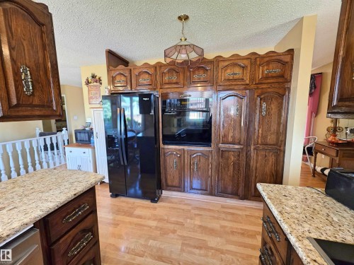 Kitchen showcasing extensive wood cabinetry, laminate flooring, built-in appliances, and granite-style countertops - 5201 54 Street, Elk Point, AB - Indoor Photo Showing Kitchen