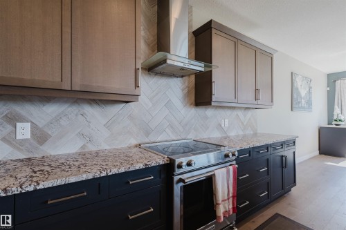 Modern kitchen featuring stainless steel appliances, granite countertops, two-tone cabinetry, and a herringbone pattern tile backsplash - 4125 Kennedy Green Sw, Edmonton, AB - Indoor Photo Showing Kitchen With Upgraded Kitchen