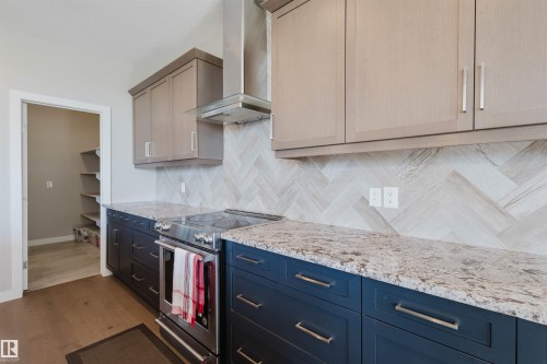 Modern kitchen featuring two-tone cabinetry with light upper and dark lower cabinets, a stainless steel range with overhead vent hood, and a herringbone pattern tile backsplash - 4125 Kennedy Green Sw, Edmonton, AB - Indoor Photo Showing Kitchen With Upgraded Kitchen