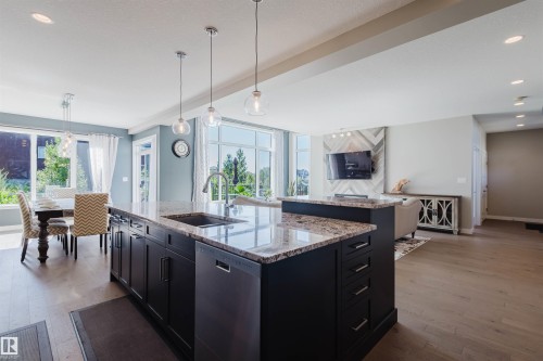 Expansive open-concept living area featuring a large kitchen island with a built-in sink and pendant lighting, wood-finish flooring, abundant natural light from large windows, and recessed ceiling lights - 4125 Kennedy Green Sw, Edmonton, AB - Indoor Photo Showing Kitchen With Upgraded Kitchen