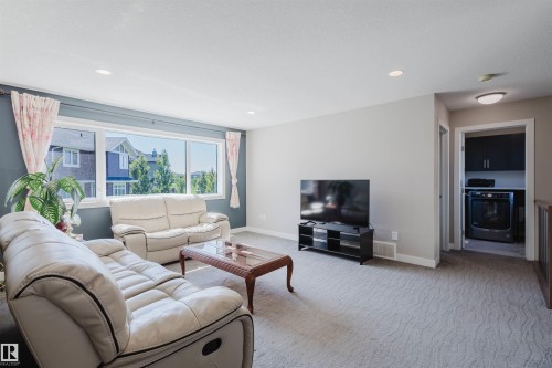 Carpeted living area featuring a large window, recessed lighting, and a dedicated laundry alcove with built-in cabinetry and an integrated washer and dryer - 4125 Kennedy Green Sw, Edmonton, AB - Indoor Photo Showing Living Room