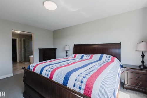 Carpeted bedroom with light gray walls, an oval flush mount ceiling light, and an open doorway revealing a bathroom with a glass-enclosed shower and a freestanding tub - 4125 Kennedy Green Sw, Edmonton, AB - Indoor Photo Showing Bedroom