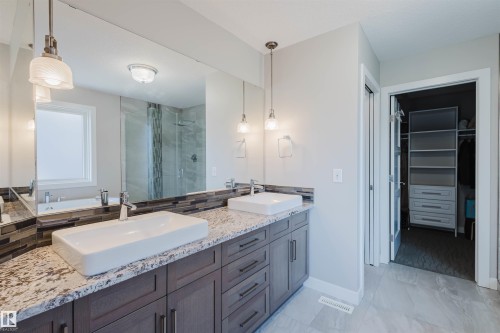 Dual vessel sinks set on a granite-finish countertop with dark wood cabinetry - 4125 Kennedy Green Sw, Edmonton, AB - Indoor Photo Showing Bathroom