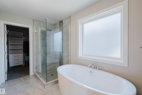Freestanding soaking tub with chrome fixtures, a spacious glass-enclosed shower with a rainfall showerhead, and a tiled shower bench - 4125 Kennedy Green Sw, Edmonton, AB - Indoor Photo Showing Bathroom