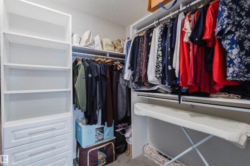 Custom white built-in closet system featuring open shelving, multiple hanging rods, and integrated drawers with horizontal pulls - 4125 Kennedy Green Sw, Edmonton, AB - Indoor With Storage
