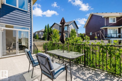 Spacious outdoor deck featuring light-toned decking, black metal railings, and vibrant green foliage - 4125 Kennedy Green Sw, Edmonton, AB - Outdoor With Deck Patio Veranda