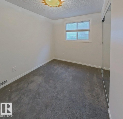 Neutral-toned room featuring a single window, grey carpet flooring, white baseboards, and mirrored closet doors - 60 Northwoods Village Nw, Edmonton, AB - Indoor Photo Showing Other Room
