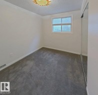 Neutral-toned room featuring a single window, grey carpet flooring, white baseboards, and mirrored closet doors - 