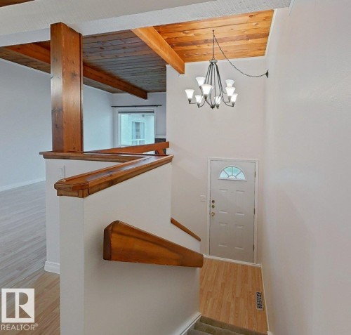 Distinctive open-concept interior showcasing exposed timber beams and vaulted wood-finish ceiling, complemented by a custom wooden staircase with built-in shelving - 60 Northwoods Village Nw, Edmonton, AB - Indoor Photo Showing Other Room