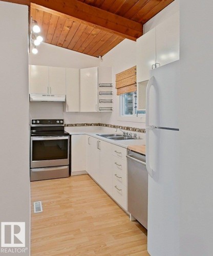 Kitchen featuring a vaulted wood-paneled ceiling, white cabinetry, stainless steel appliances, light-toned wood-finish flooring, and a double basin sink - 60 Northwoods Village Nw, Edmonton, AB - Indoor Photo Showing Kitchen With Double Sink